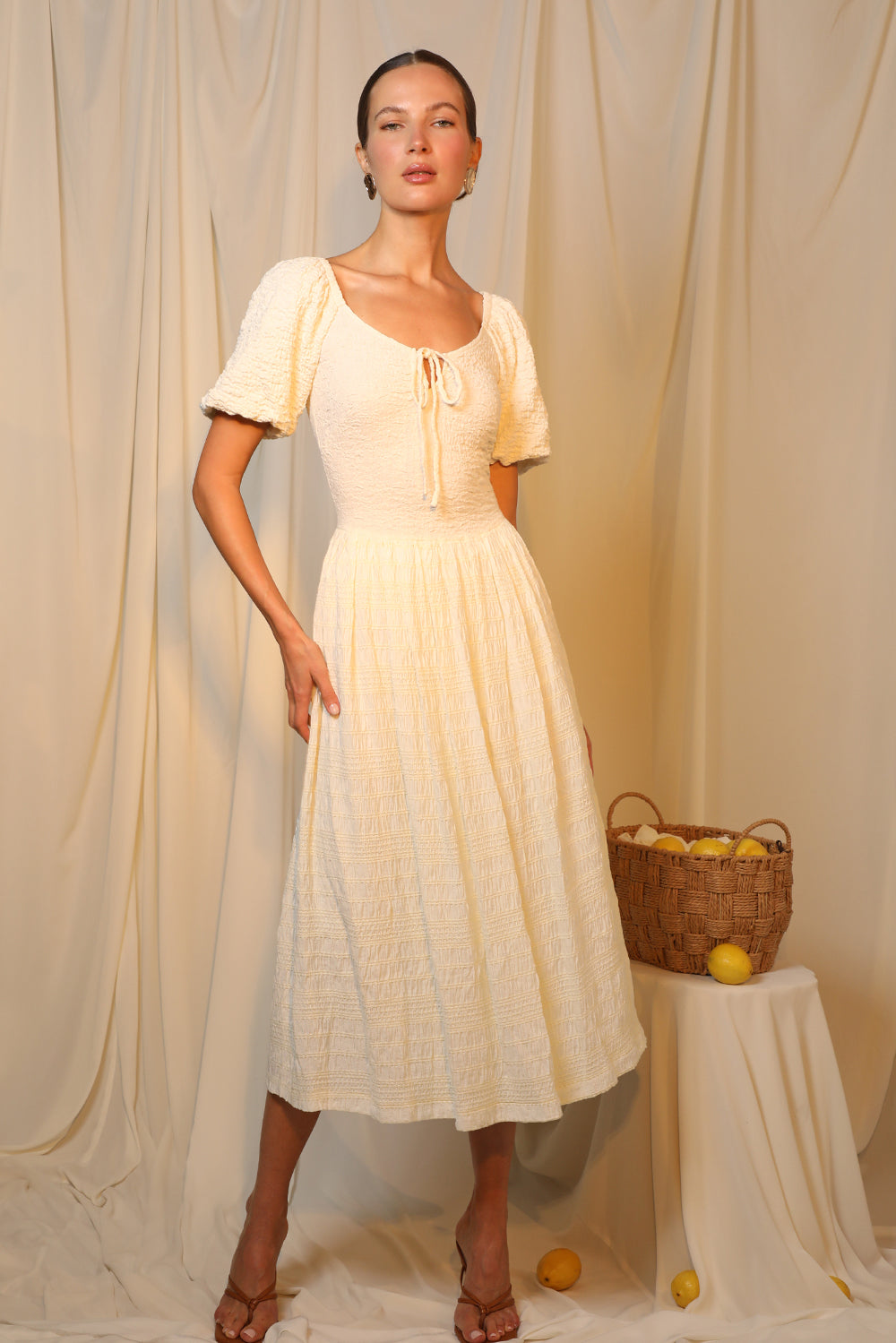 Model wears a cream, popcorn-textured midi dress with balloon sleeves and a tied neckline.