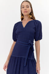 Close -up of model wearing navy, midi dress. Bodice features a tie belt and a V-neckline. The short sleeves are puffed.