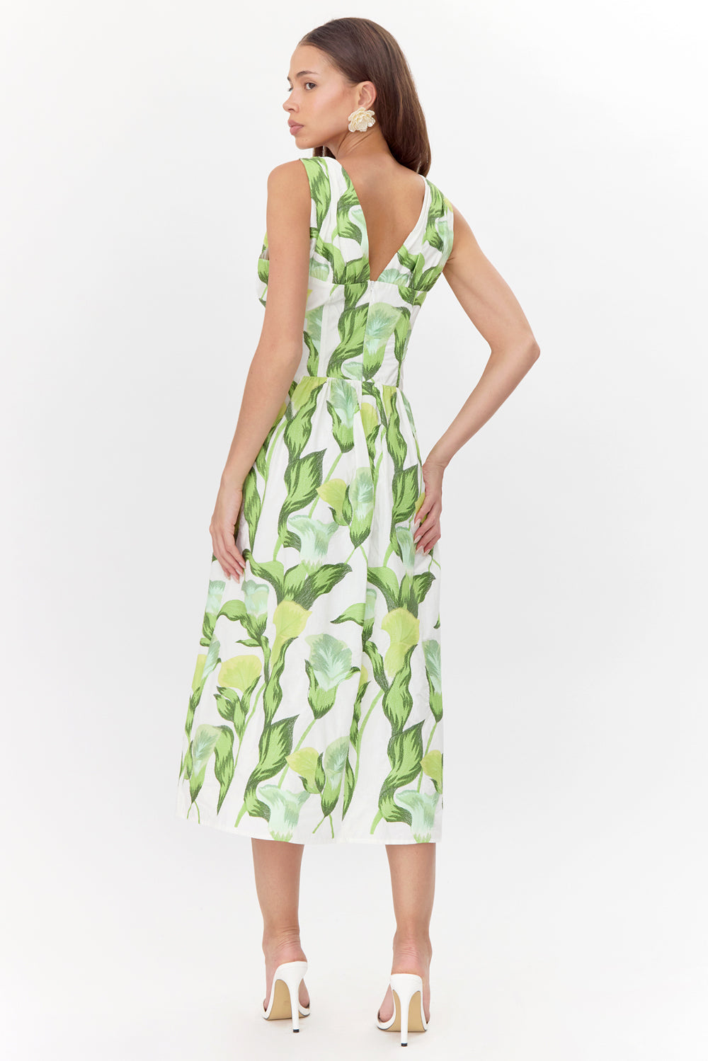 Model wears a sleeveless midi dress. The dress has a white base with a green floral print. The dress features a V-backline.