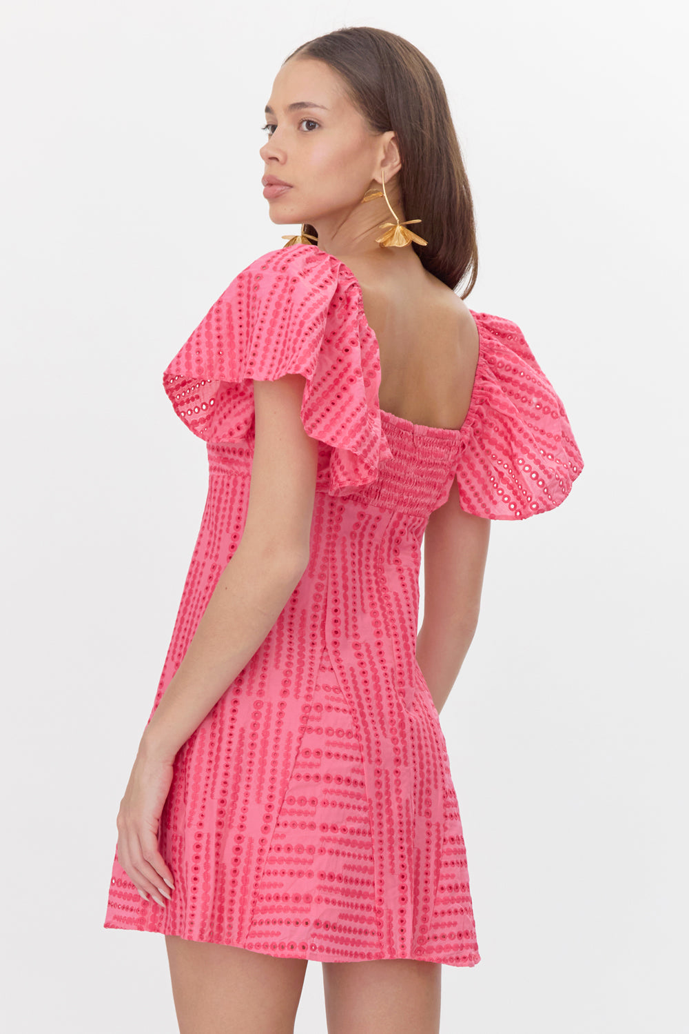 Back view of model wearing pink mini dress with embroidered polka dots. The dress features a smocked panel.