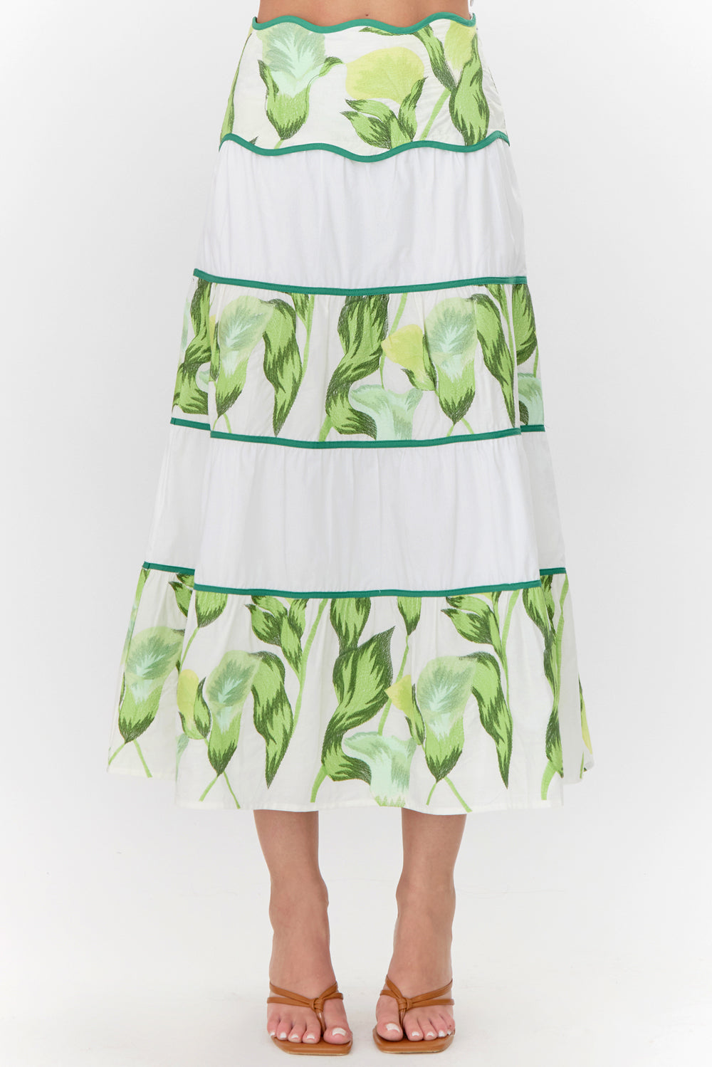 Close-up view of midi skirt. The skirt has a white base and has contrasting tiers. The tiers feature a green floral print.